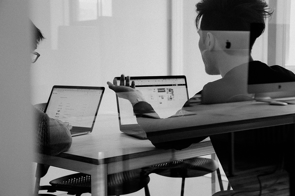 Two people seated at a table working on laptops during a business strategy meeting, with the heading 'Strategy' and text describing expert guidance for business growth through targeted marketing, small positioning, and actionable insights